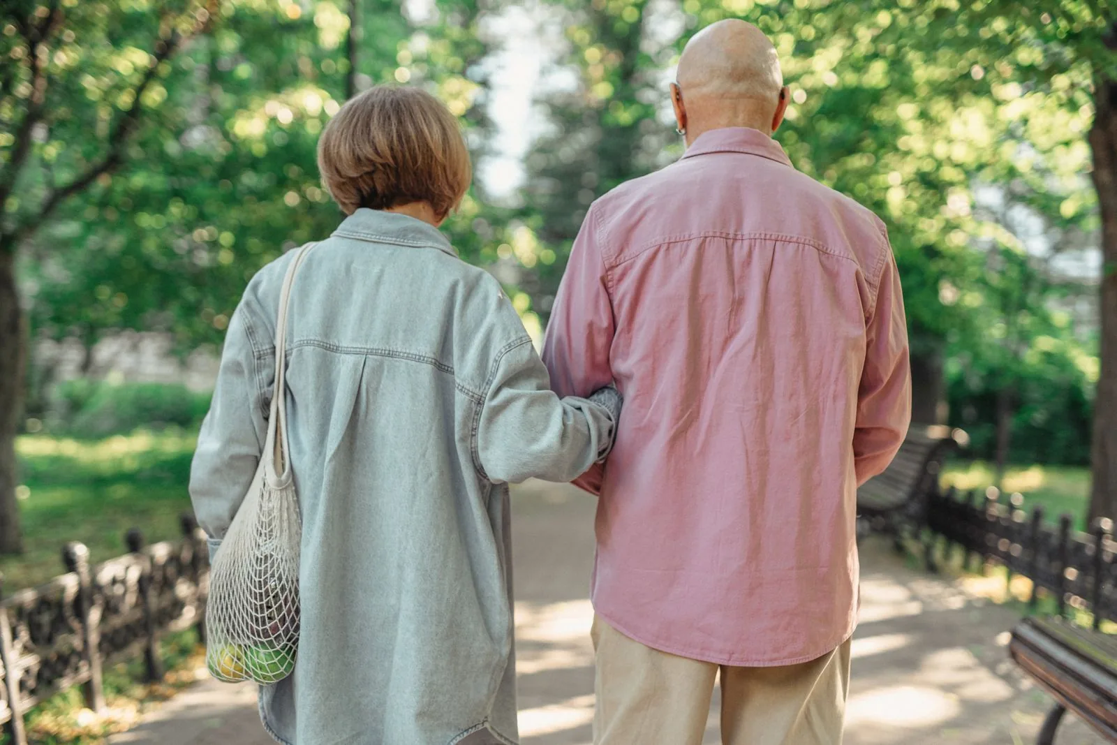 Two adults walking arm in arm along a green, tree-lined path.